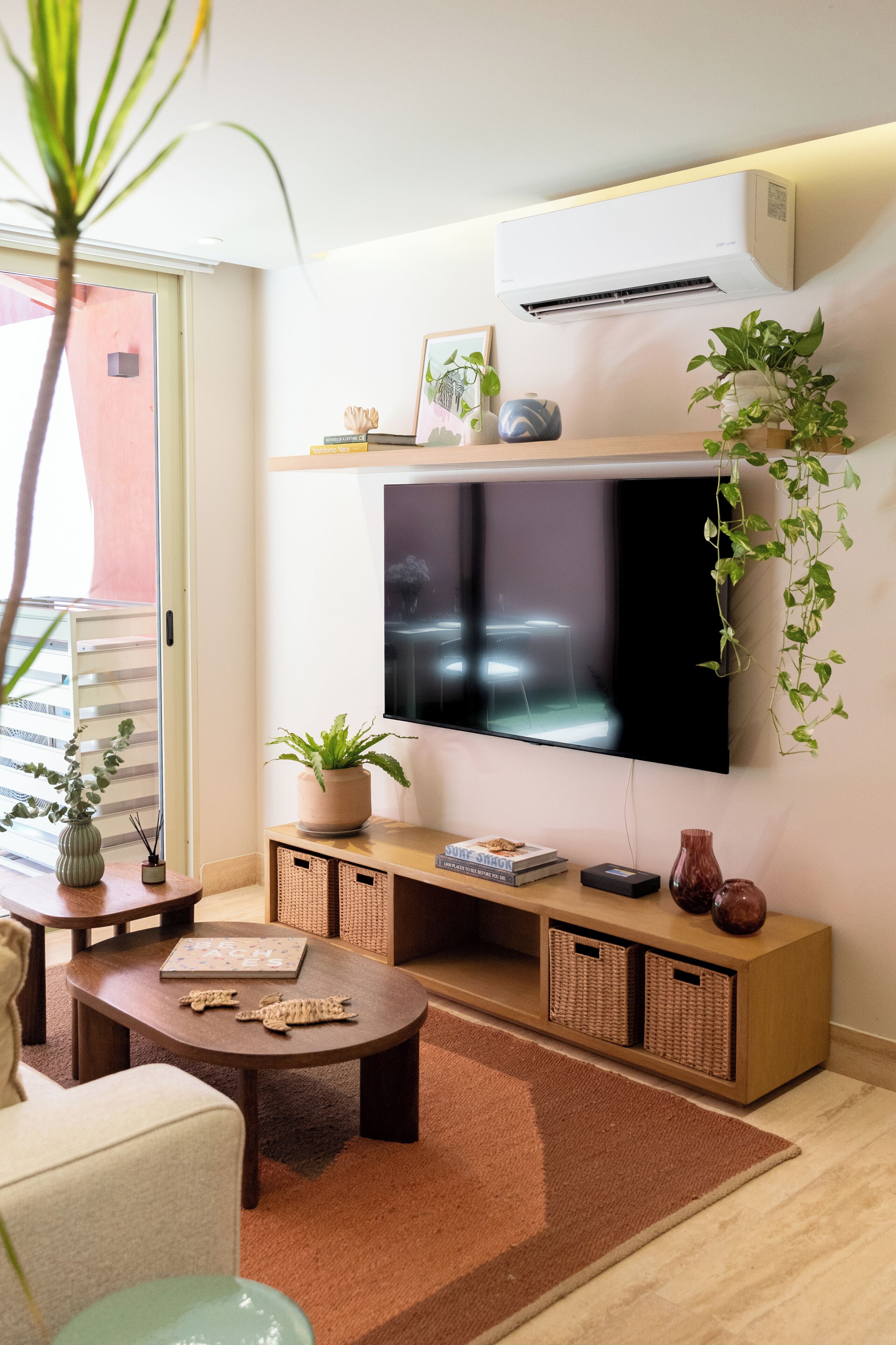 Una sala de estar con un televisor de pantalla plana montado en la pared, una mesa de centro, un sofá, una planta en maceta y una pequeña estantería.