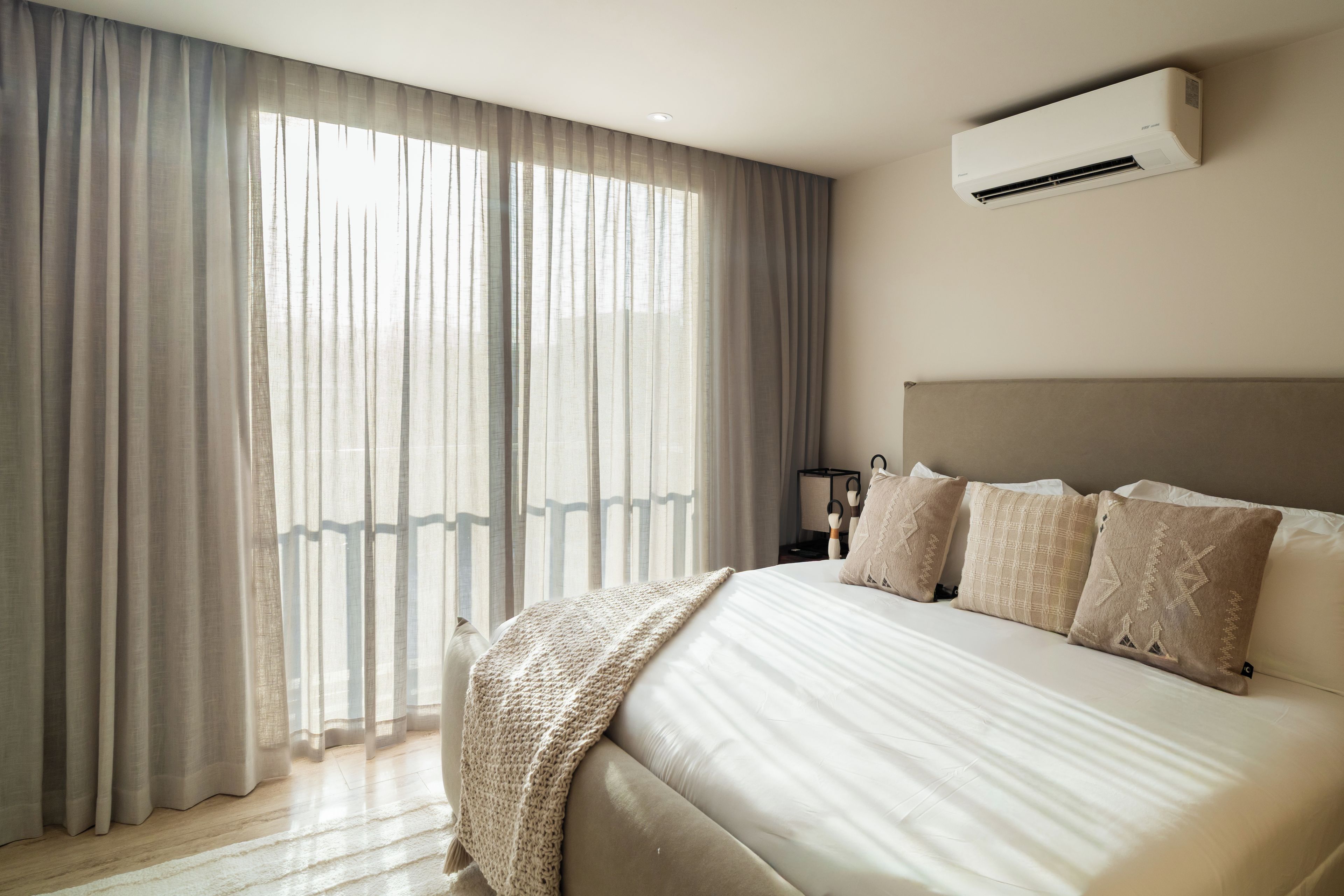 A modern bedroom with a large bed, a headboard, and an air conditioning unit.