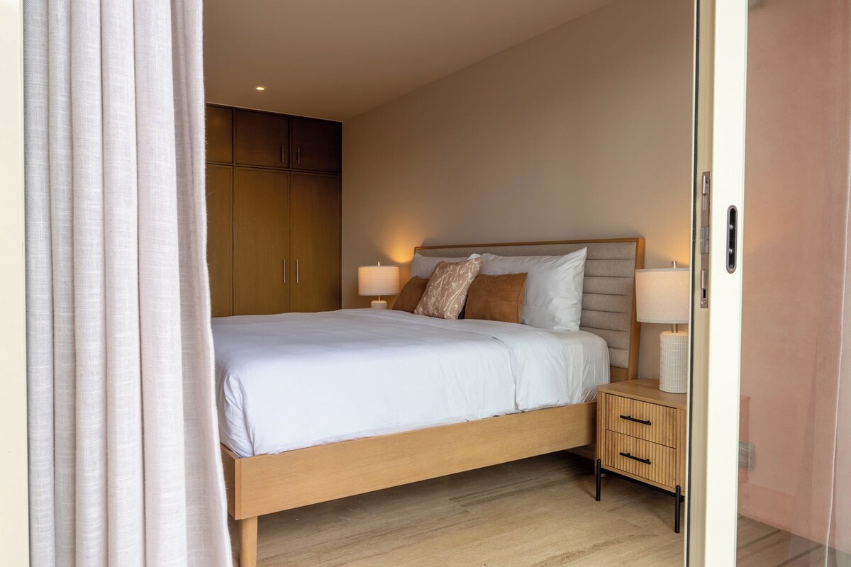 Una habitación de hotel con una cama grande, mesitas de noche, un armario y una puerta.