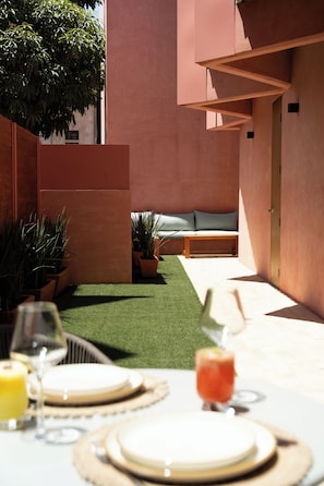 An outdoor dining area with a table set for two, surrounded by potted plants and a green lawn.
