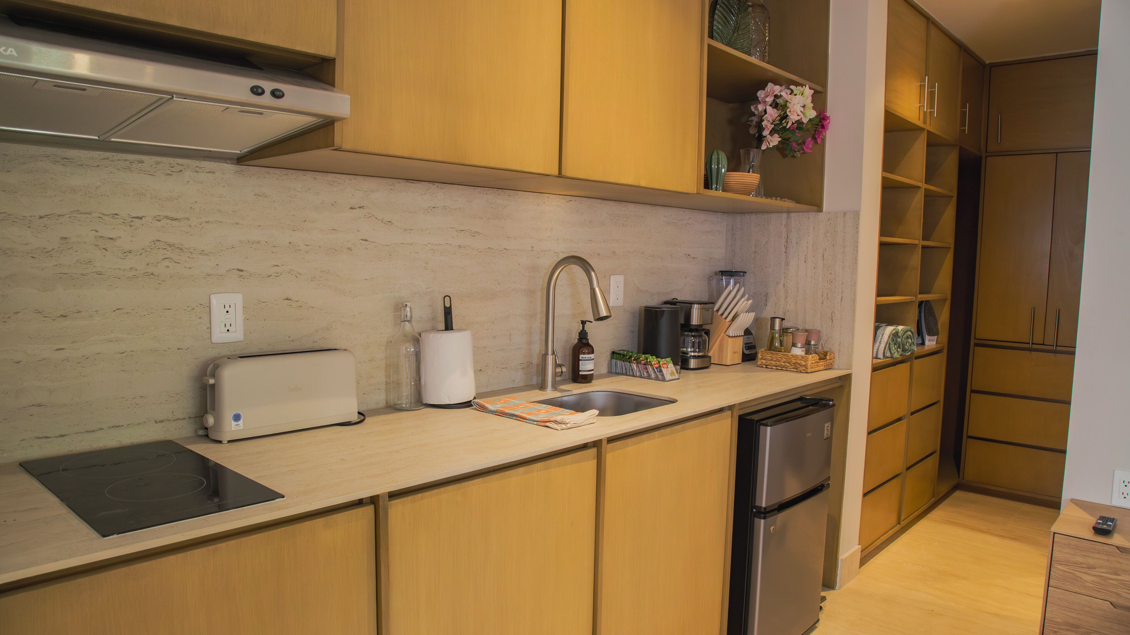A modern kitchen with wooden cabinets, a stainless steel refrigerator, a built-in oven, and a sink with a faucet.