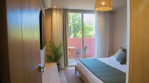 Un dormitorio con cama, mesita de noche, planta en maceta y vistas al exterior.