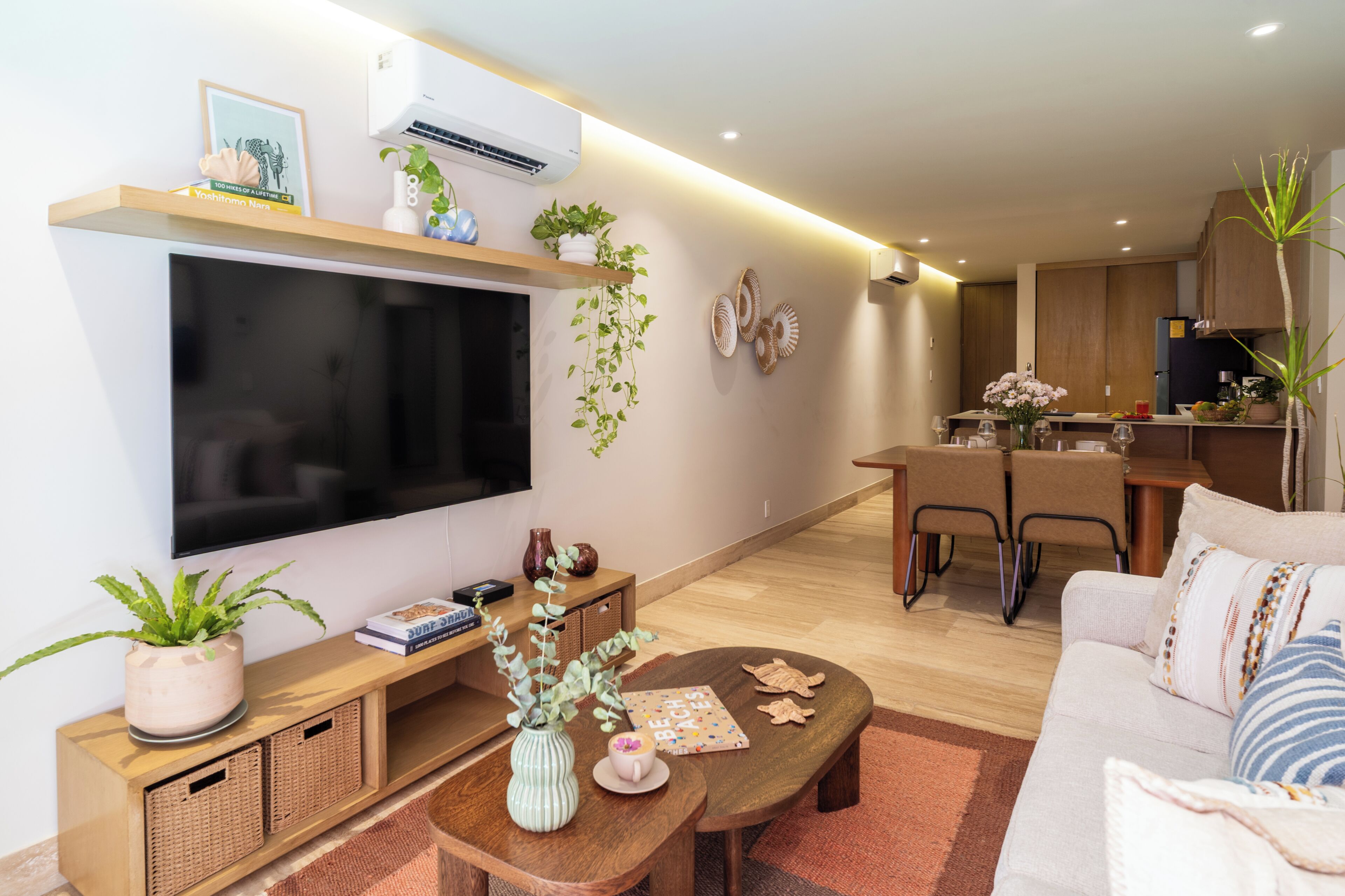 A modern living room with a flat-screen TV, a sofa, a coffee table, and a dining area with chairs.