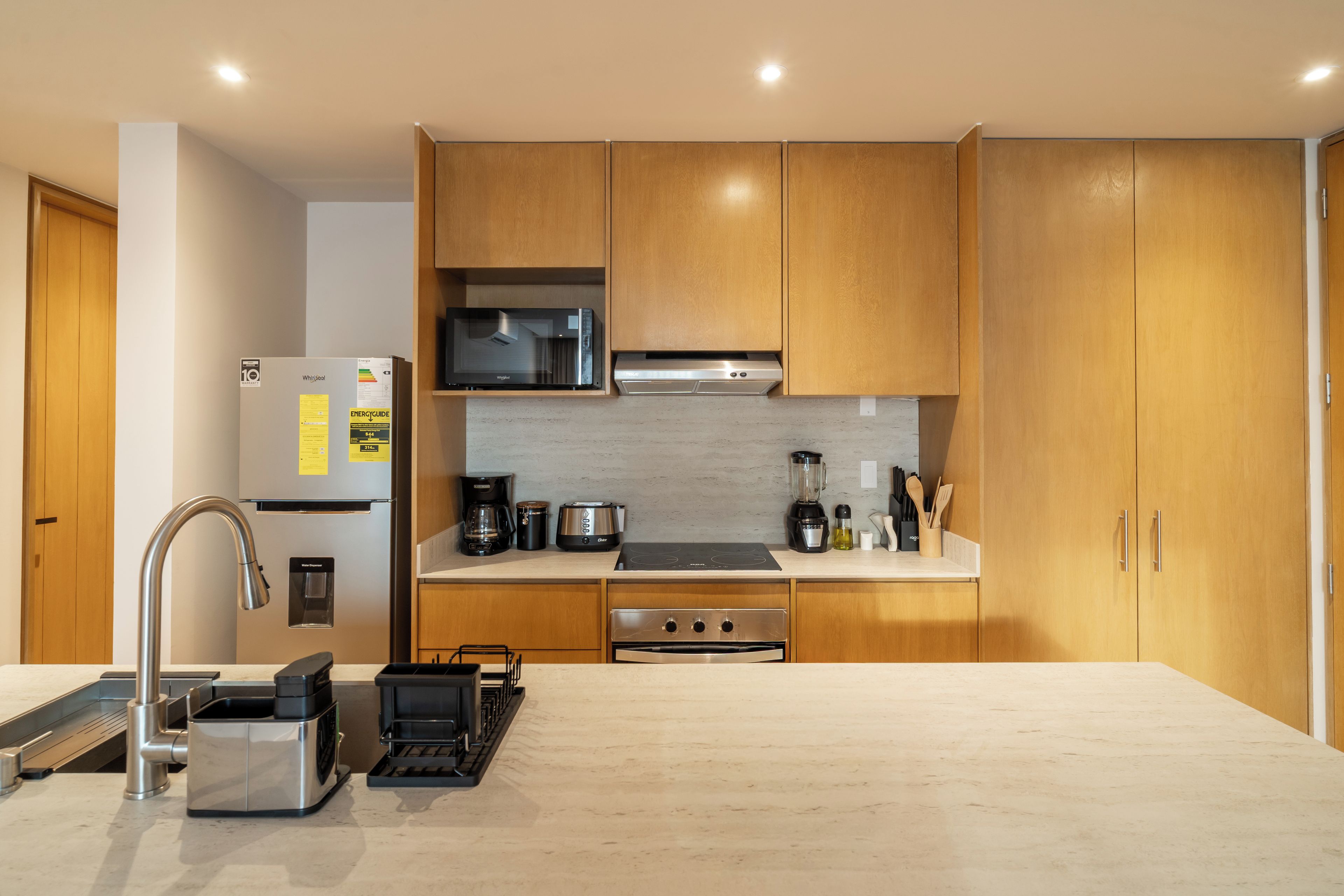 A modern kitchen with wooden cabinets, a built-in microwave, a coffee maker, and a water dispenser.