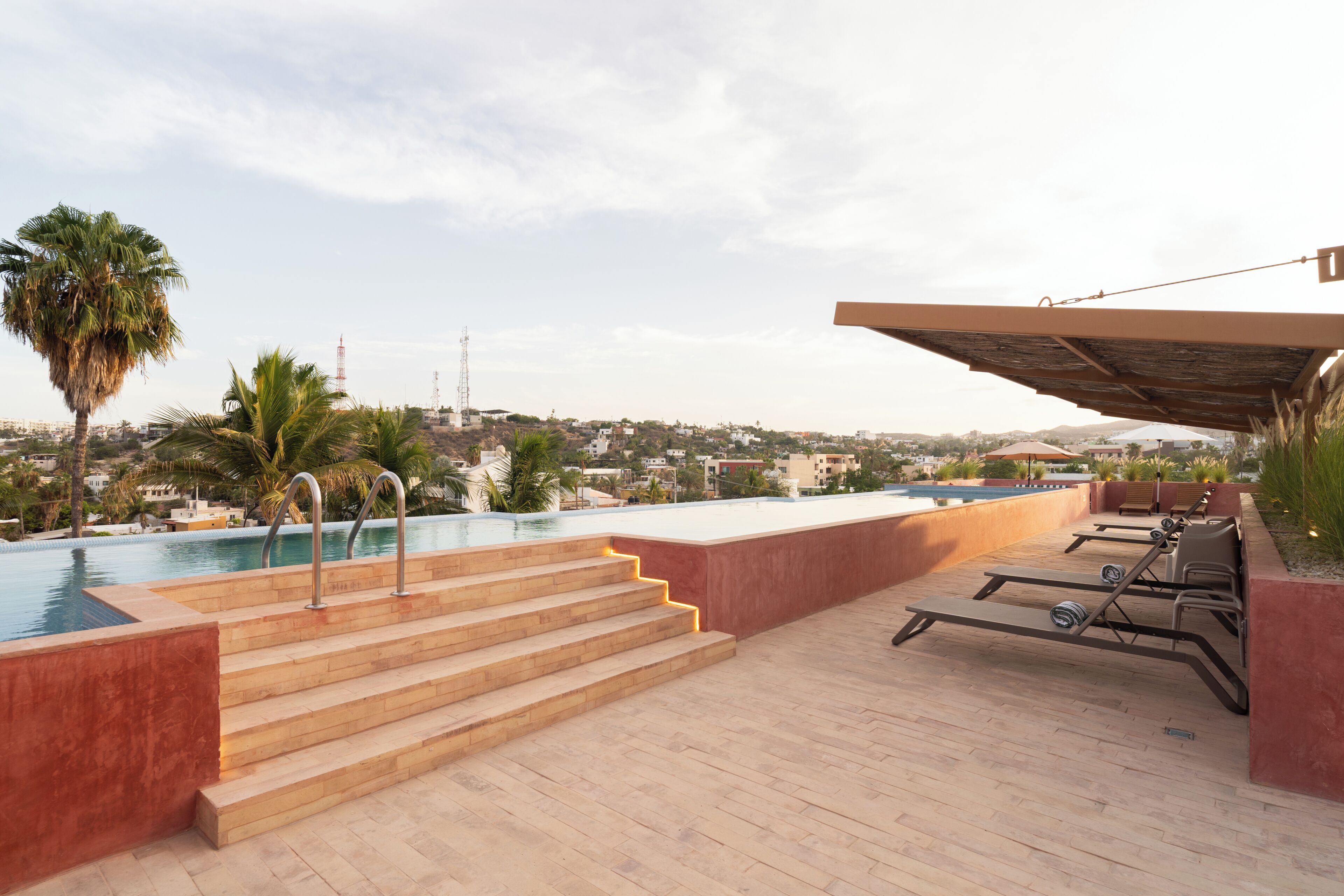 A rooftop pool area with steps leading to the water, lounge chairs, and a view of the cityscape.