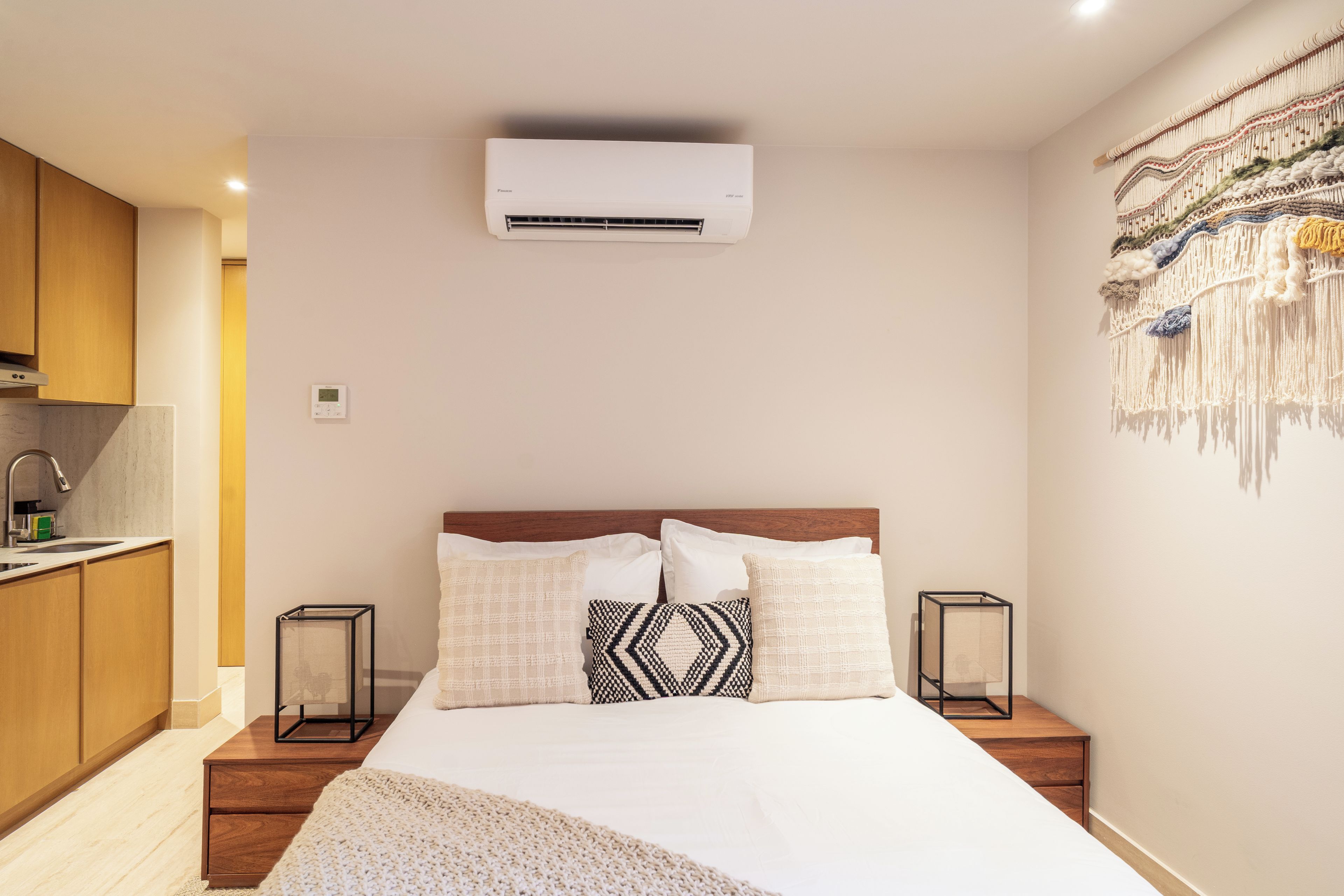 Une chambre d’hôtel comprenant un lit, des tables de chevet, un climatiseur fixé au mur, un coin cuisine et un élément décoratif mural.