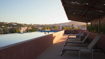 Zona de piscina en la azotea con sillones de descanso y vistas a un pueblo en la colina.