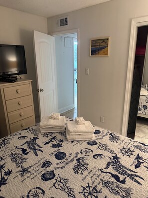 Ein Schlafzimmer mit einem Bett, einer Kommode, einem Fernseher und einer Tür zu einem anderen Raum.