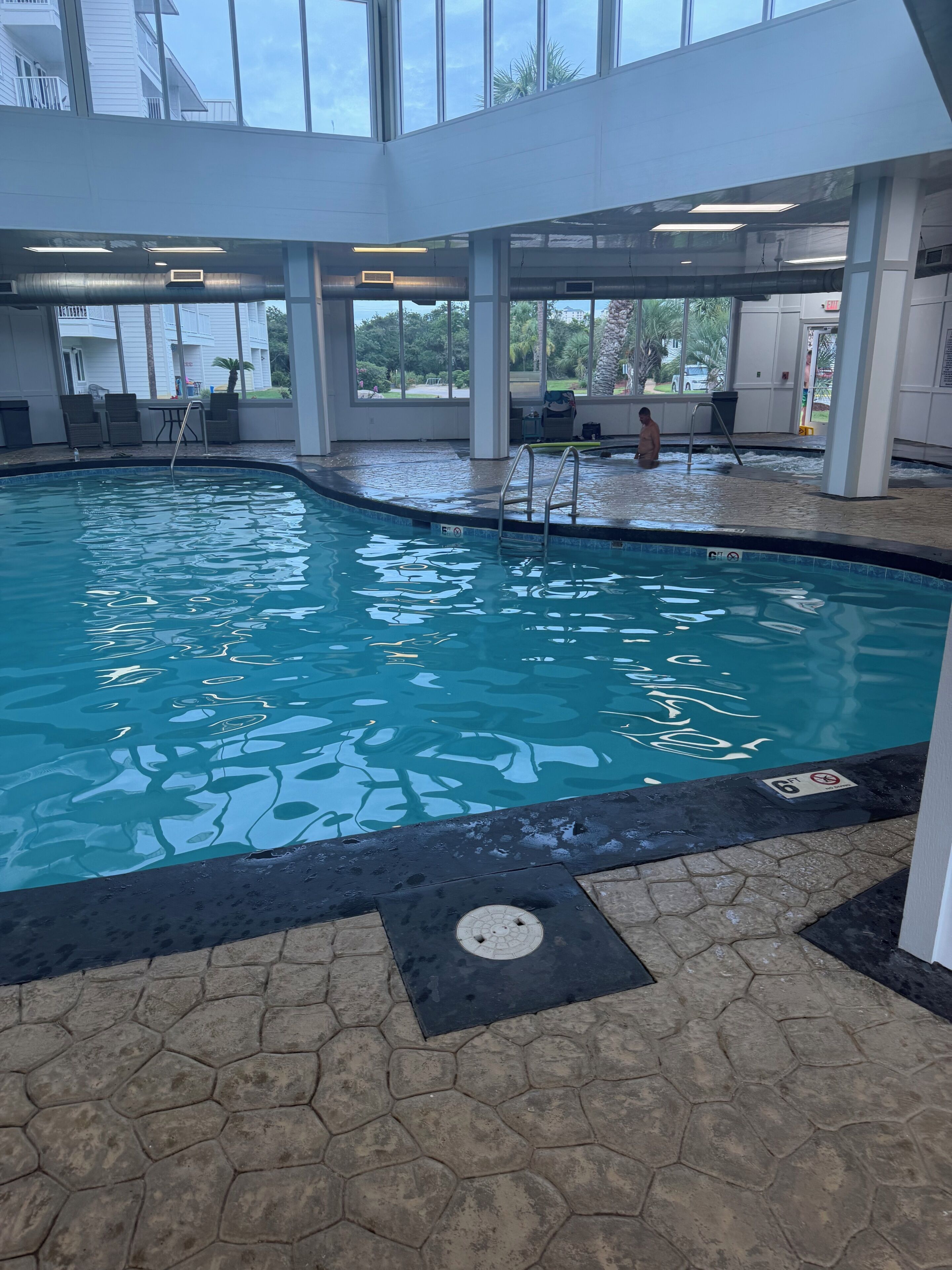 An indoor swimming pool with clear water, a lifeguard chair, and a view of the outside through large windows.