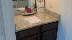 A kitchen with granite countertops, dark wooden cabinets, a hanging light fixture, and a decorative anchor sign.