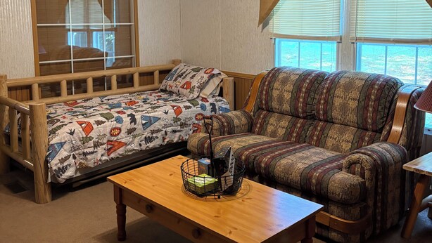 A room with a bed, a sofa, a wooden coffee table, and a ceiling fan.