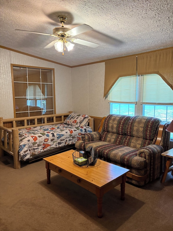 A room with a bed, a sofa, a wooden coffee table, and a ceiling fan.