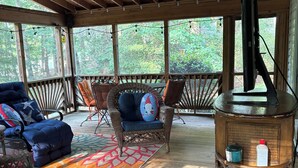 A covered outdoor seating area with wicker furniture, a patterned rug, and a wooden pillar with a television.