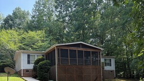 A single-story house with a fenced porch, a satellite dish, and a small shed in a wooded area.