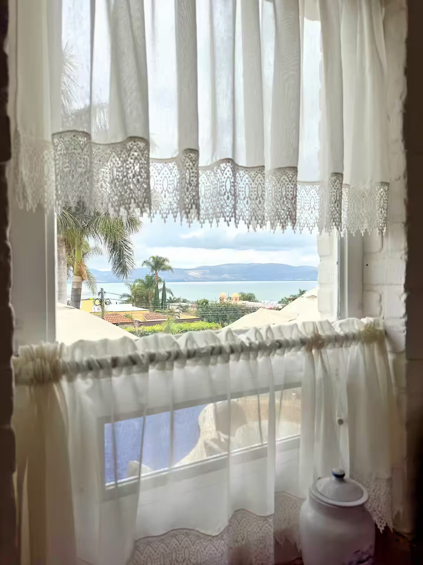 Una ventana con cortinas blancas y vista a un paisaje costero.