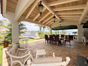 An outdoor patio with wooden beams, a pool, and seating.