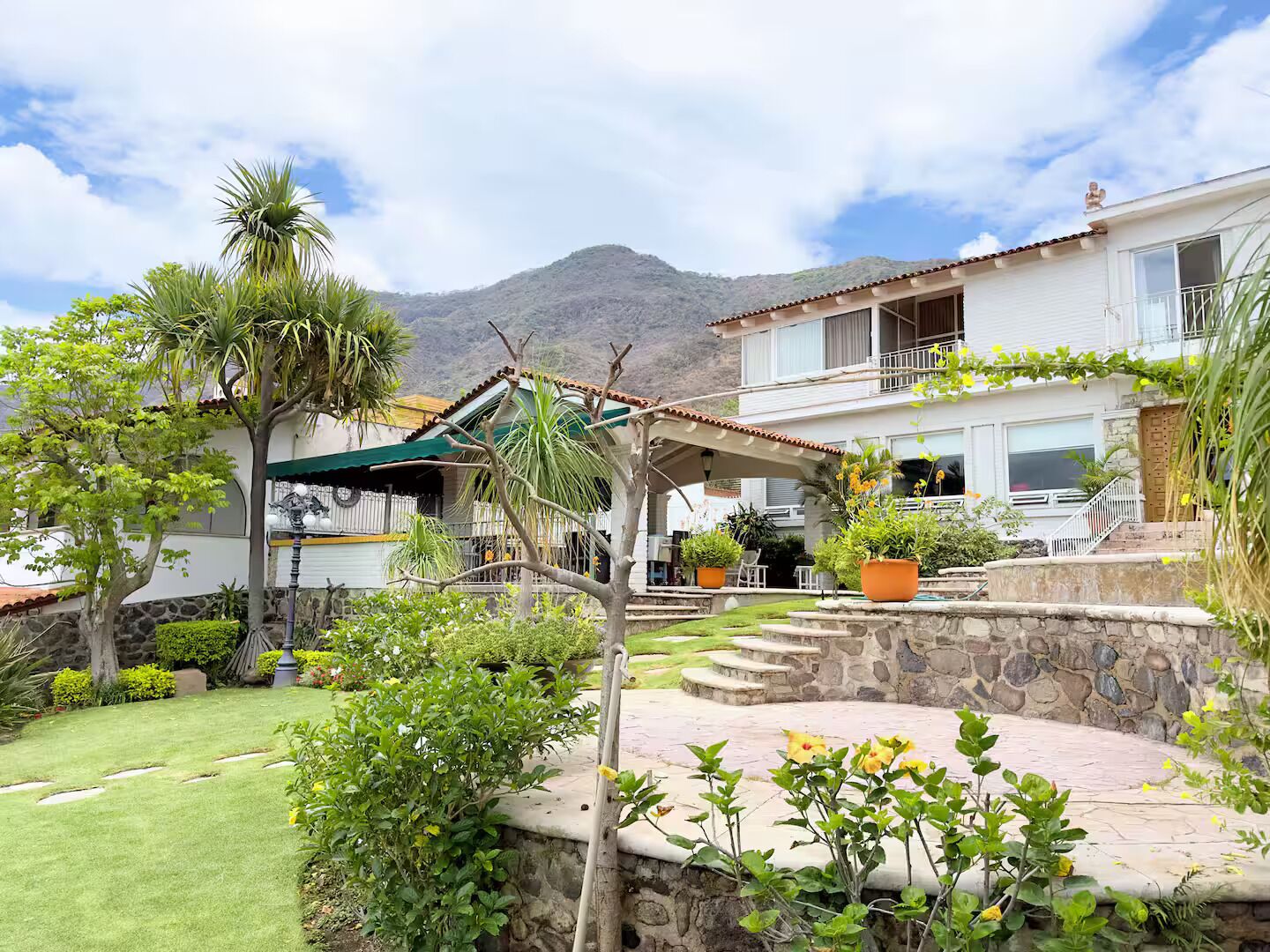 A two-story house with a stone wall, a covered patio, and a mountain in the background.
