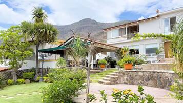 A two-story house with a stone wall, a covered patio, and a mountain in the background.