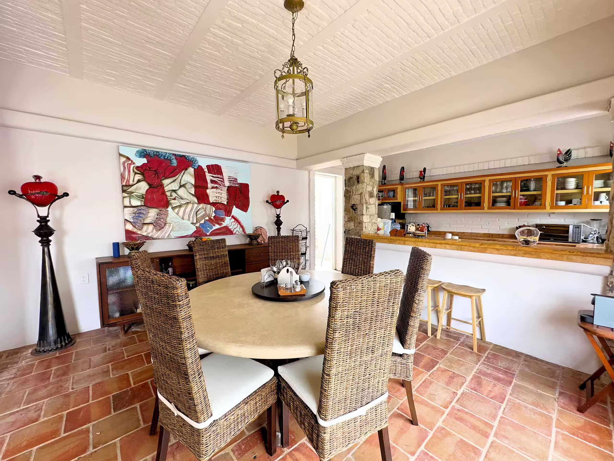 A dining area with wicker chairs, a round table, and a kitchen with wooden cabinets.
