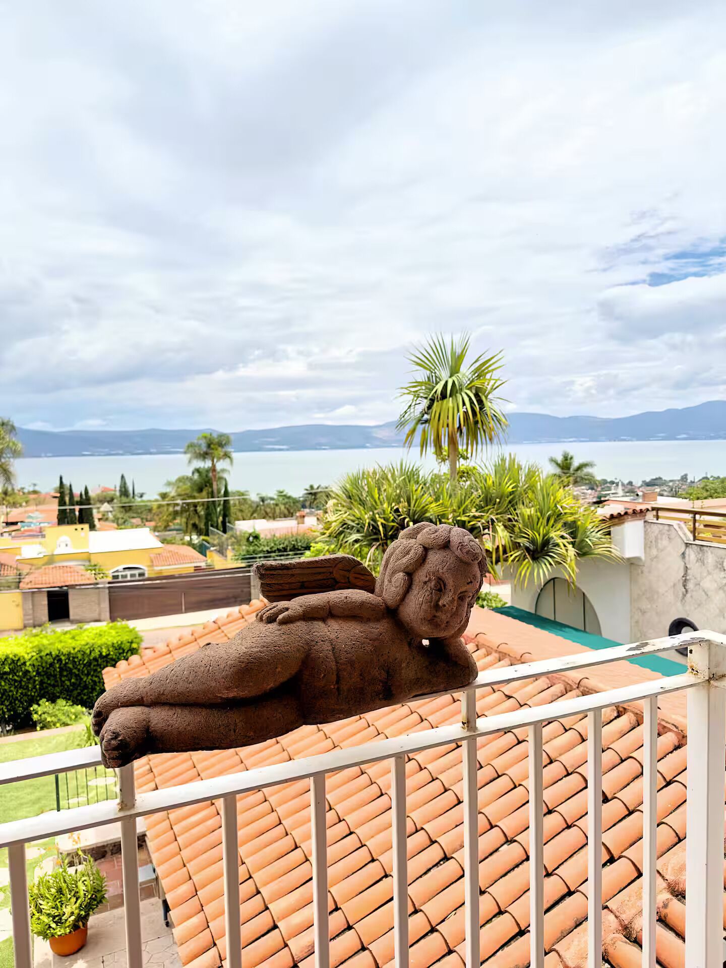 A balcony with a teddy bear sculpture, a view of a body of water, and a distant mountain range.