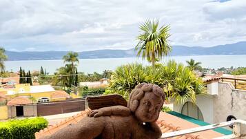 A balcony with a teddy bear sculpture, a view of a body of water, and a distant mountain range.