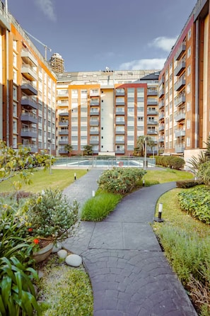 Ein mehrstöckiges Wohngebäude mit Balkonen, einem gepflasterten Gehweg und einer angelegten Gartenanlage.