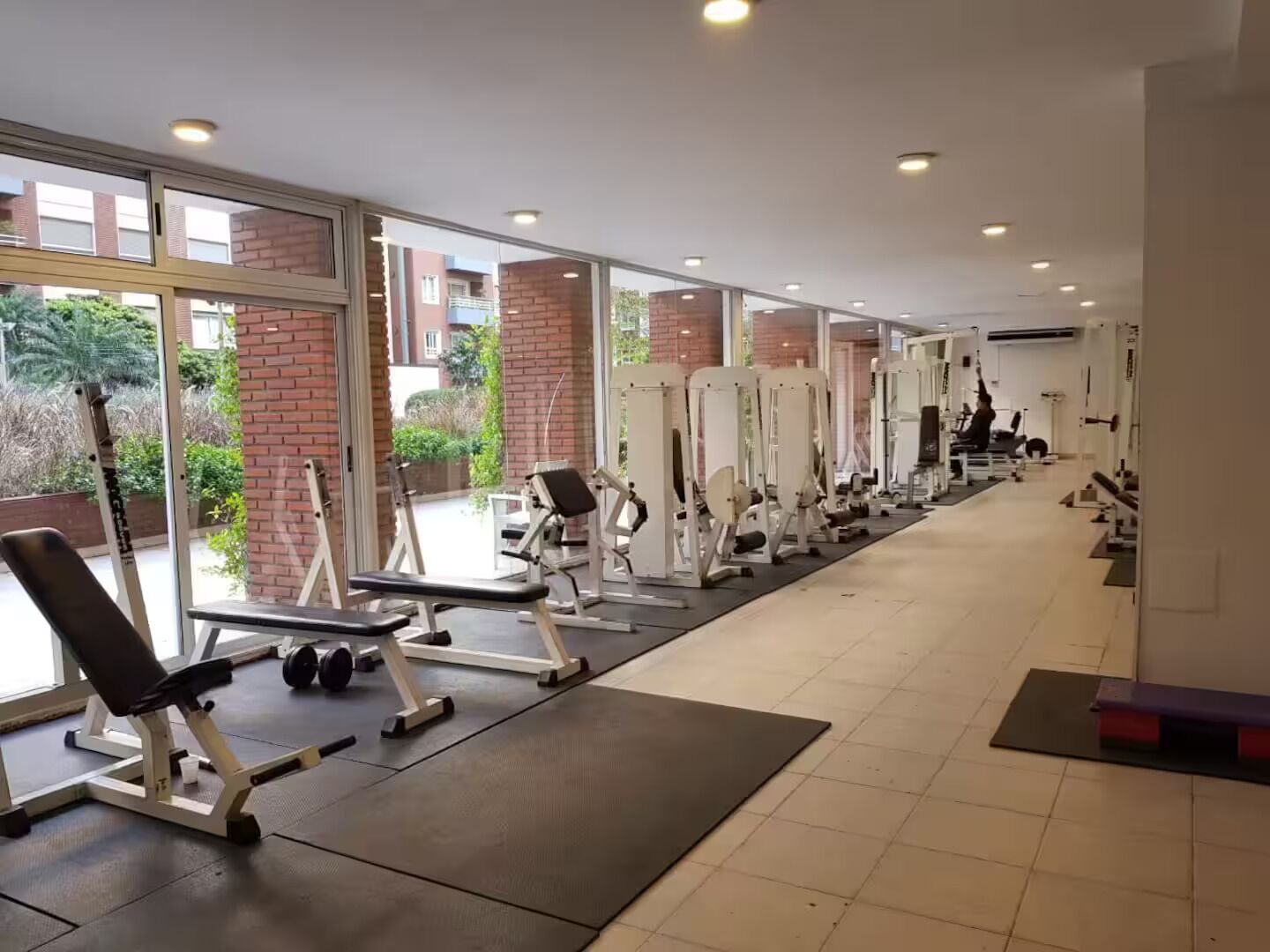 Une salle de sport équipée de divers appareils d’exercice, dotée de grandes fenêtres et offrant une vue sur l’extérieur.