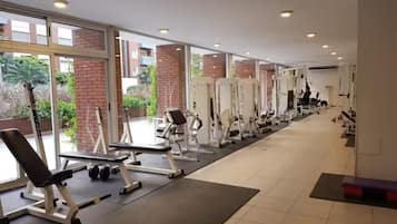 Une salle de sport équipée de divers appareils d’exercice, dotée de grandes fenêtres et offrant une vue sur l’extérieur.