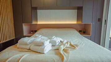 A neatly made bed with folded towels, a bedside table, and a wall-mounted shelf.