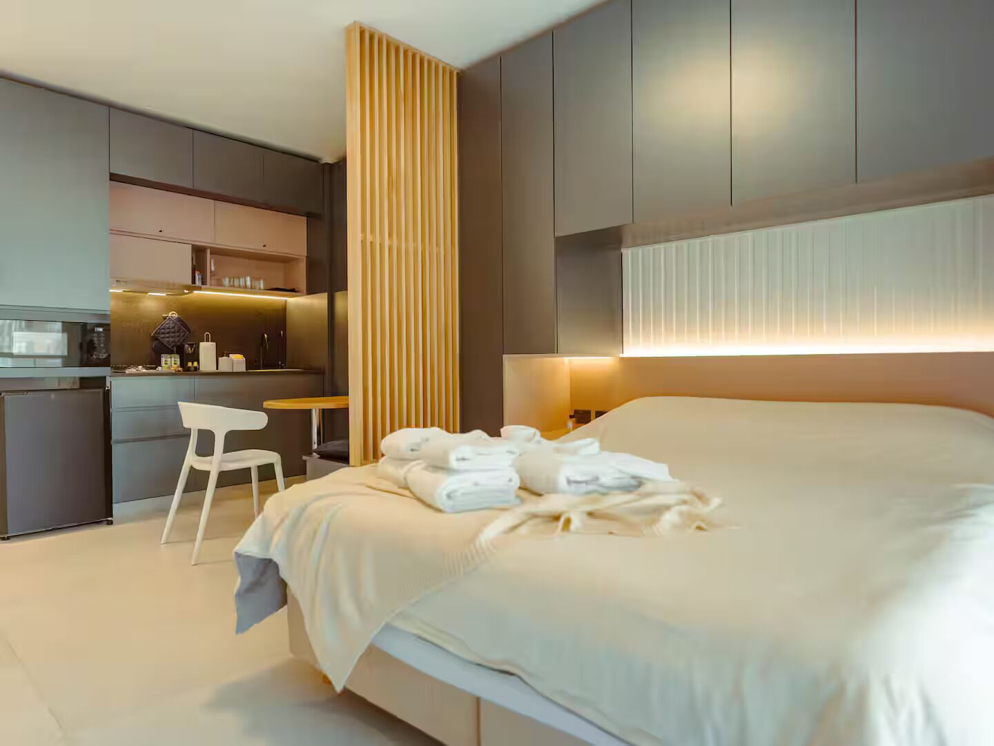 A modern hotel room with a bed, a desk, and a kitchenette.