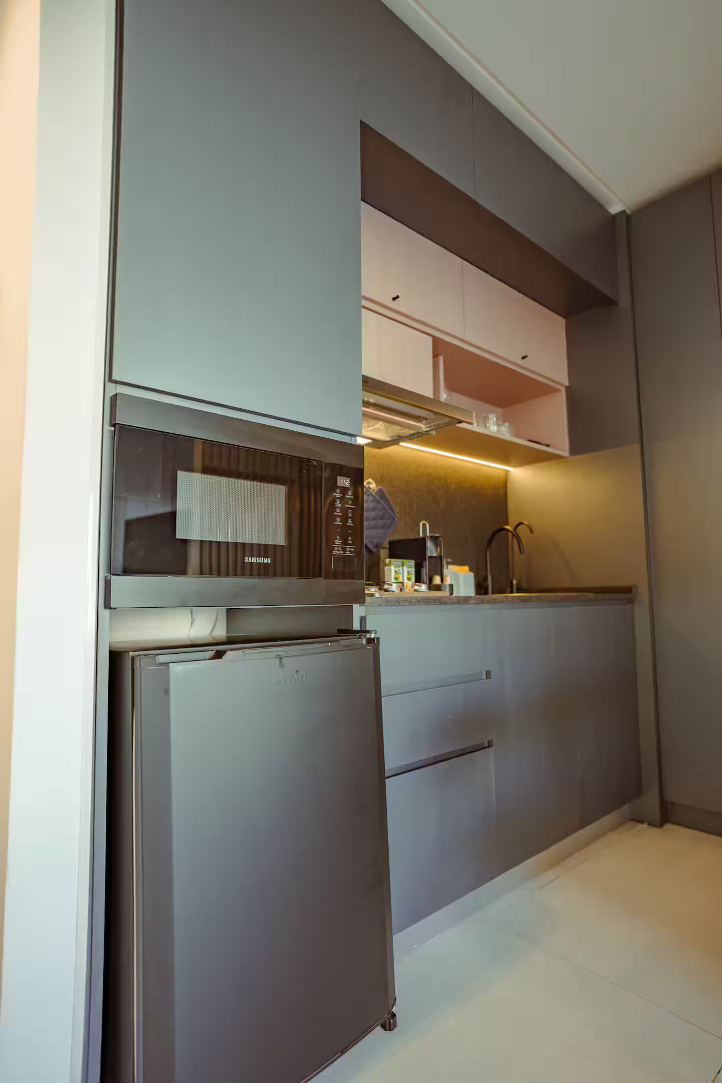 A modern kitchen with a built-in microwave, refrigerator, and a countertop with a coffee maker.