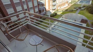 Ein Balkon mit Korbmöbeln und einem Glastisch, mit Blick auf ein Wohngebiet mit Gebäuden und Grünfläche.