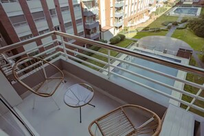 Ein Balkon mit Korbmöbeln und einem Glastisch, mit Blick auf ein Wohngebiet mit Gebäuden und Grünfläche.