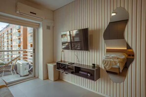 Een moderne hotelkamer met een grote televisie, een spiegelwand, een balkon met een stoel en een zichtbaar stadsgezicht.