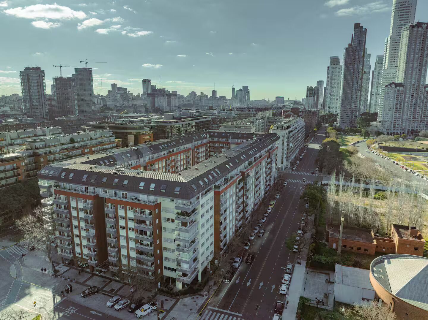 Un edificio residencial alto con varios pisos, un estacionamiento y una calle con vehículos.