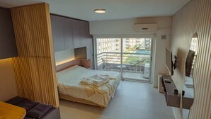 Ein modernes Hotelzimmer mit Bett, Schreibtisch, Fernseher und einem Balkon mit Stadtblick.
