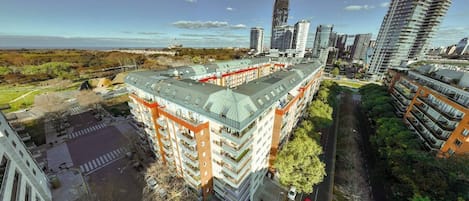 A multi-story building with a flat roof, surrounded by greenery and other high-rise buildings.