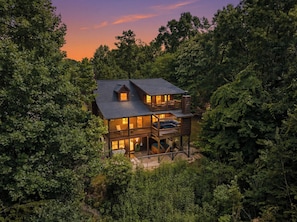 Eine zweistöckige Holzhütte, umgeben von dichtem Wald, mit einem Balkon im oberen Bereich.