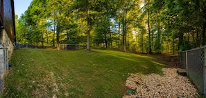 A fenced yard with a grassy area, trees, and a stone building. - Hoot Owl Lodge - Views, Bark Park, Arcade, Hot Tub (Blue Ridge)