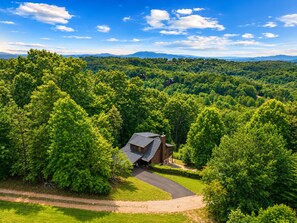 Une propriété rurale avec une allée sinueuse, entourée d’une forêt dense et bordée, au loin, par une chaîne de montagnes.