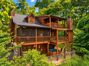 A two-story wooden cabin with a balcony, a hot tub, and a stone foundation. - Hoot Owl Lodge - Views, Bark Park, Arcade, Hot Tub (Blue Ridge)