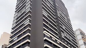 A modern high-rise building with a prominent entrance and a green sign indicating the name of the building. - Studio próximo a Sirio Libanês  (São Paulo)