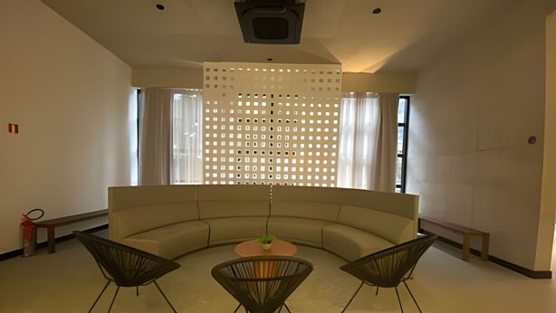 A modern living room with a curved sofa, three black chairs, a small table with a plant, and a decorative screen. - Studio próximo a Sirio Libanês  (São Paulo)