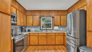 Una cocina con armarios de madera, electrodomésticos de acero inoxidable y una ventana con vista a la vegetación.