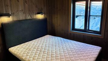 Una habitación con cama, paredes de madera, ventana con vistas y una lámpara en el techo.