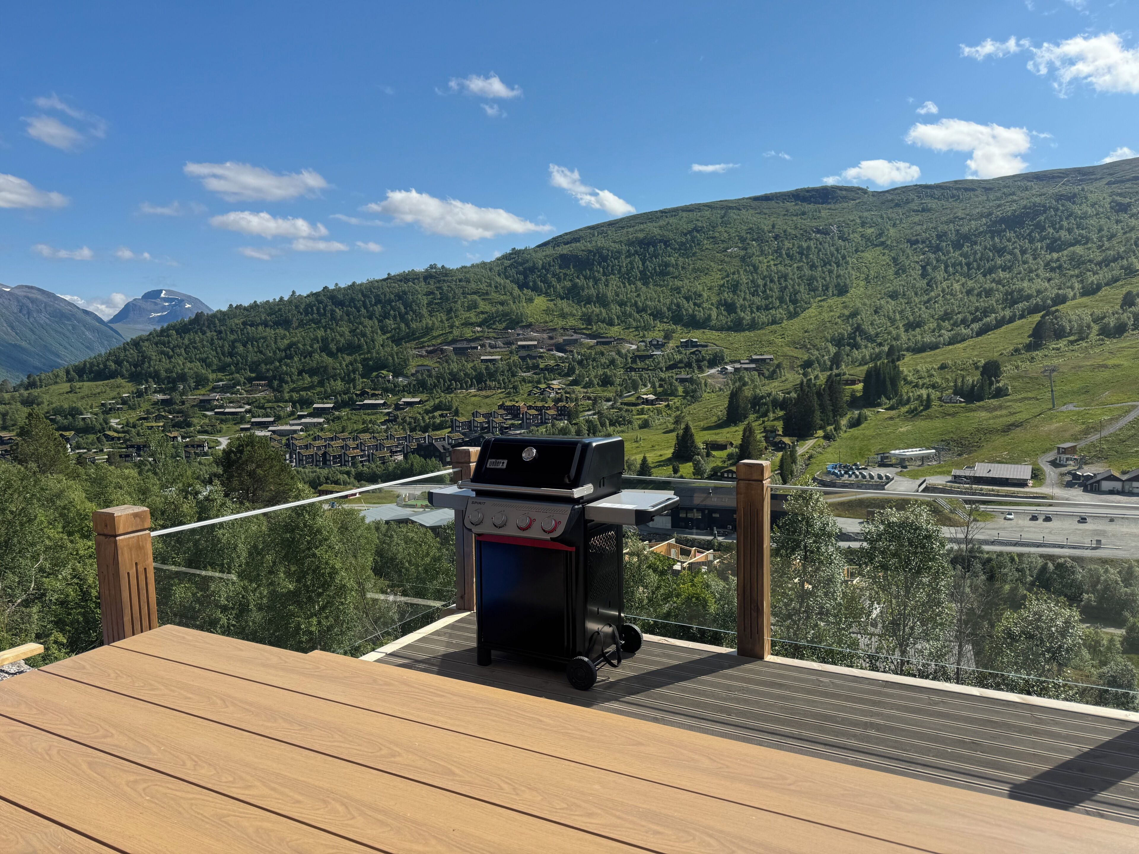 A wooden deck with a barbecue grill overlooking a mountainous landscape with a village below.
