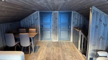 Une pièce avec un plafond en pente, un plancher en bois, une table à manger avec des chaises et deux portes.