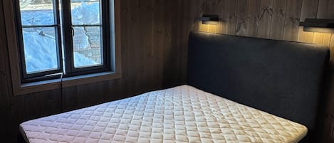 A room with a bed, wooden walls, a window with a view of snow, and a hanging light fixture.