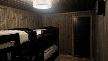 A room with wooden walls and a ceiling, featuring two bunk beds and a door.