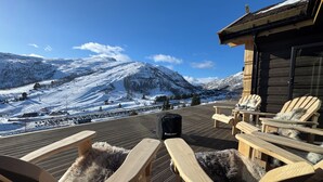 Een houten terras met Adirondack-stoelen, met uitzicht op een besneeuwd berglandschap.
